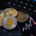 Gold Bitcoin and Ethereum cryptocurrency coins with candle stick graph chart, laptop keyboard, and digital background.